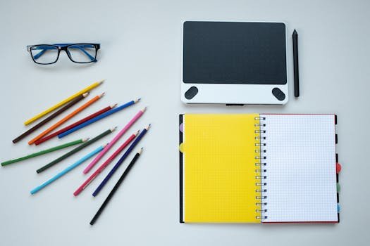 Flat lay of a creative workspace featuring colored pencils, notebook, and graphic tablet.