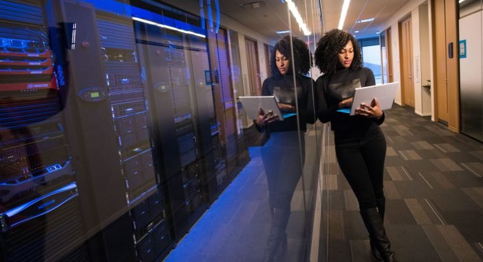 A woman using a laptop navigating a contemporary data center with mirrored servers.